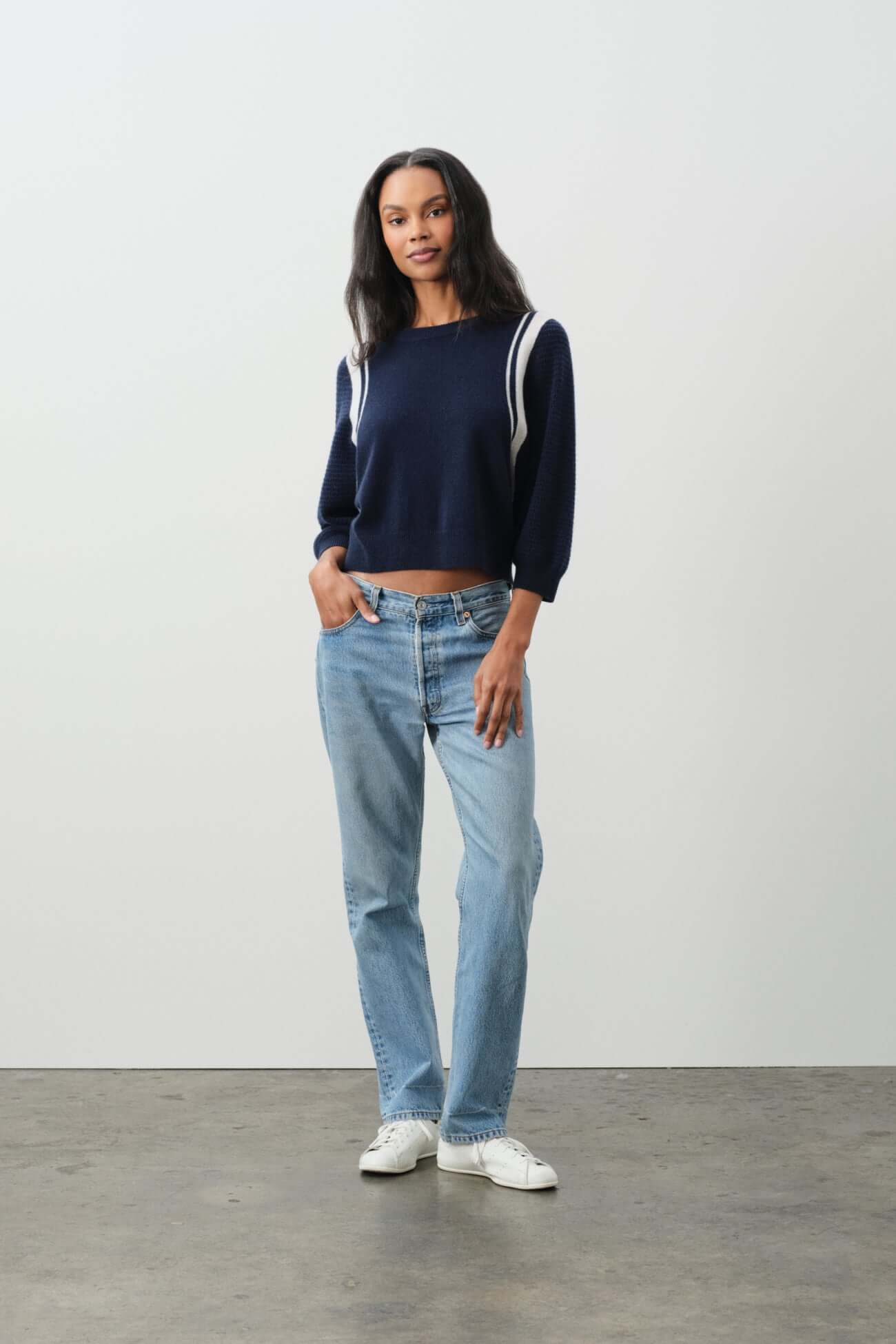 Model wearing stylish navy sweater and blue jeans showcasing trendy Tops collection.