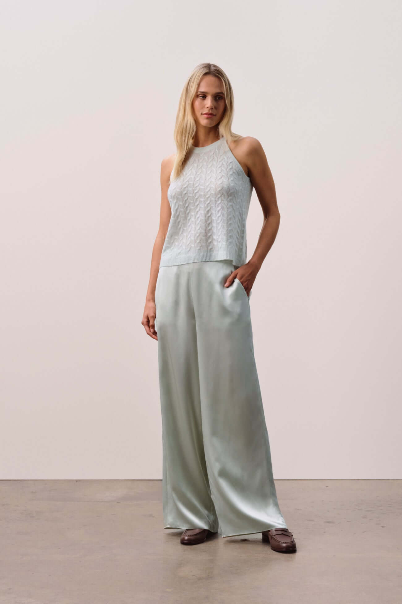 Model wearing a stylish outfit with a light sweater and wide-leg pants in a minimalist setting.